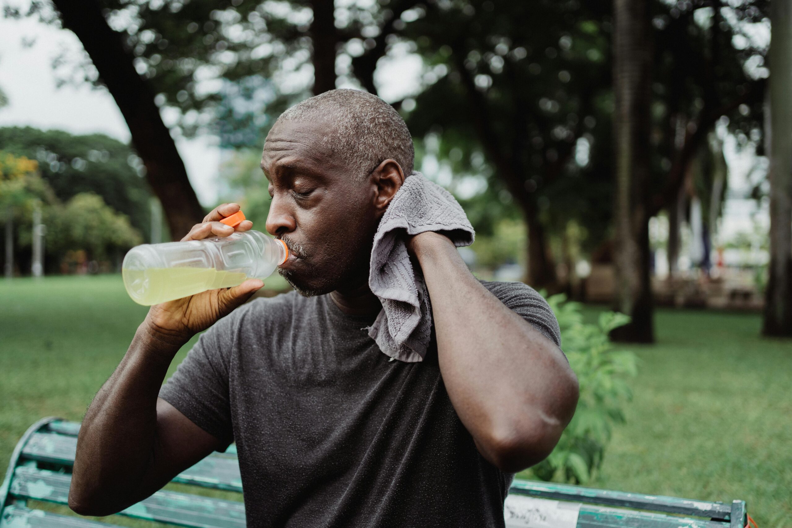 Middle-aged man in park hydrating with a sports drink, cooling down after workout.